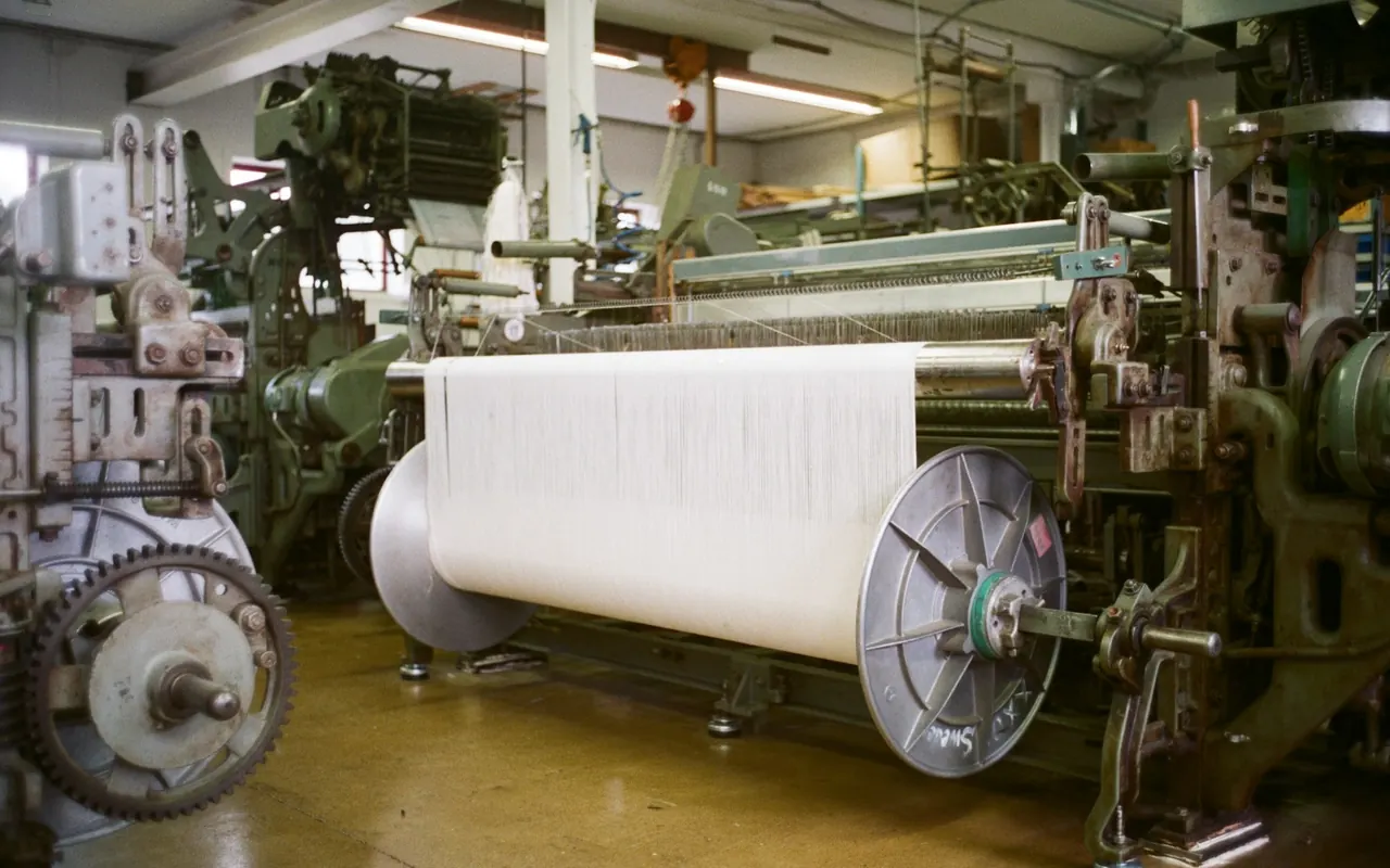 Weaving loom with a roll of white fabric in a textile mill